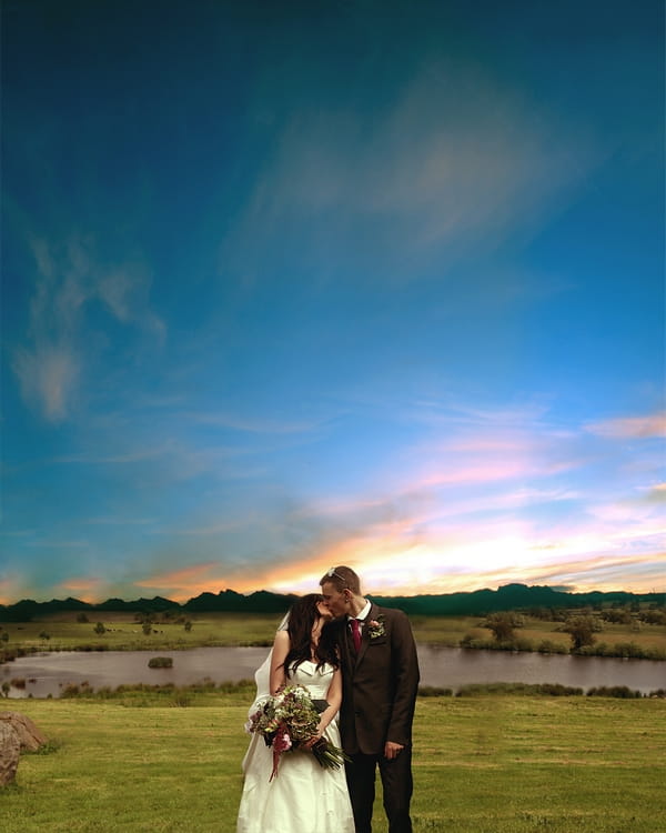 Bride and groom kiss in front of beautiful sky