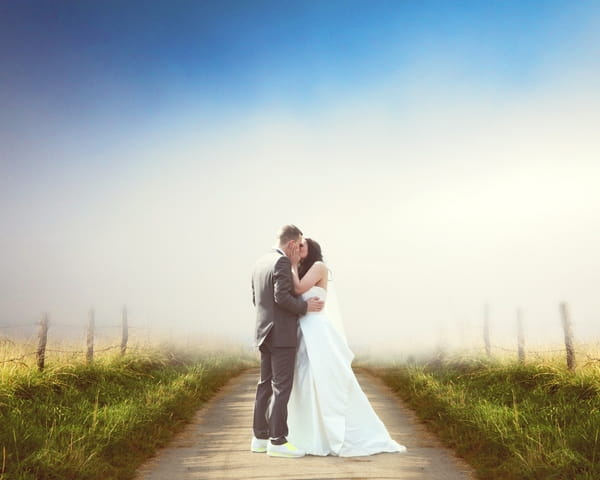 Bride and groom kiss on long country road