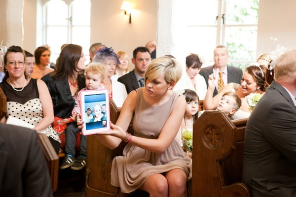 Wedding guest holding out iPad to show ceremony on webcam
