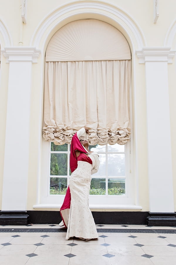 Bride with red-lined long wedding coat standing in front of window