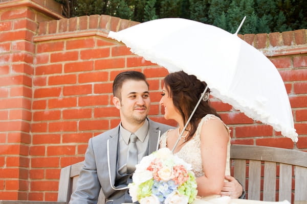 Bride and groom sitting on bench under umbrella