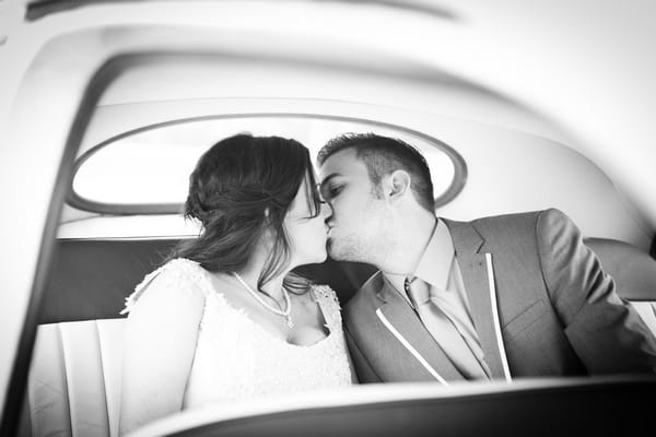 Bride and groom kiss in back of wedding car