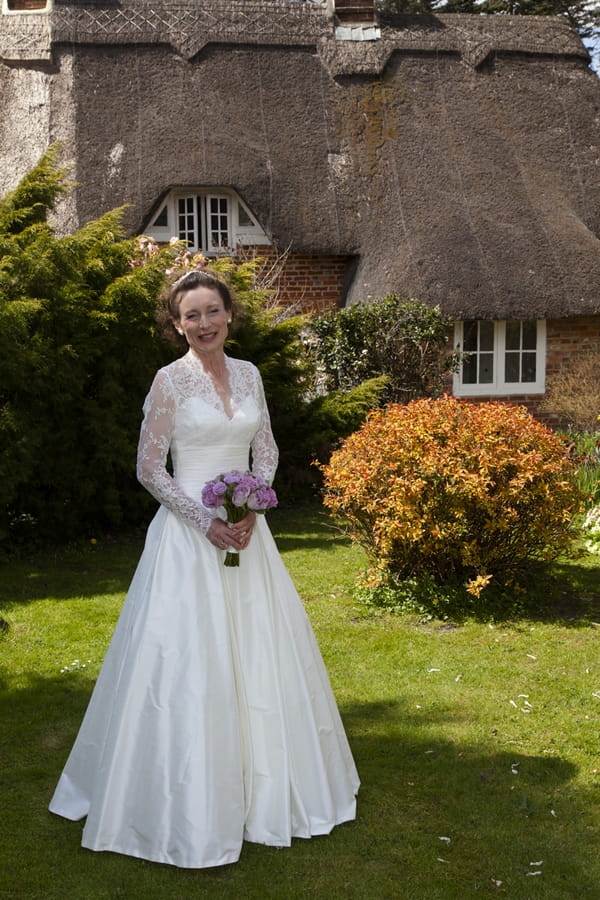 Bride standing in front of thatched cottage