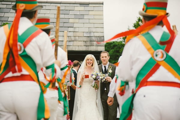 Bride and groom walking past Morris Dancers