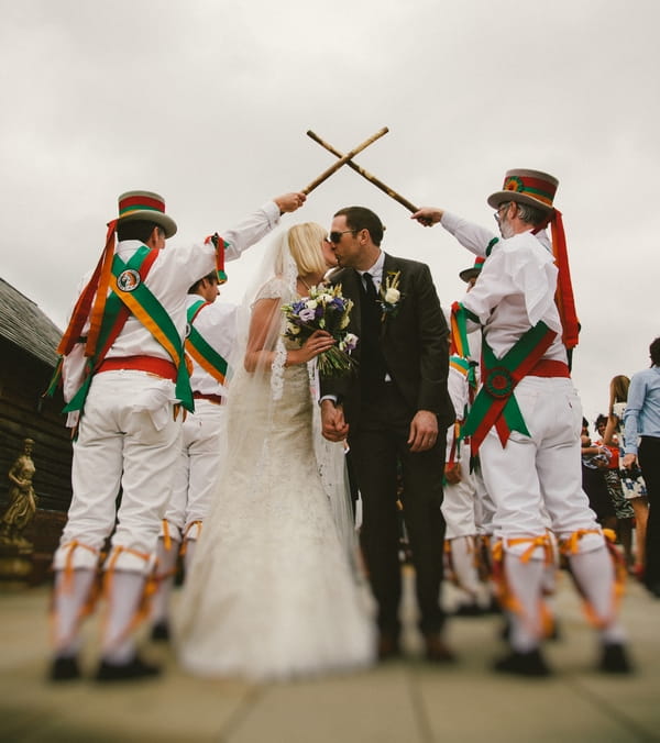 Bride and groom kiss under Morris Dancers' guard of honour