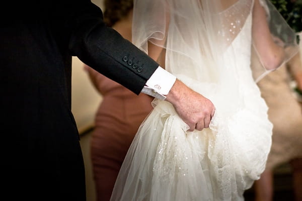 Father holding up back of bride's dress