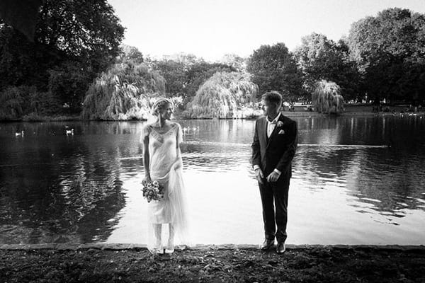 Bride and groom standing up straight in front of a lake