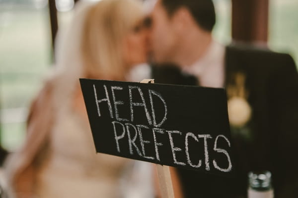 Bride and groom kiss behind wedding table sign