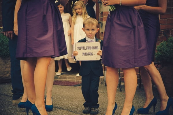 Page boy holding Here Comes the Bride sign