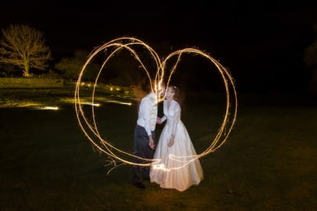 Bride and groom kssing behind heart made with sparkler