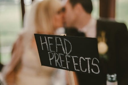 Bride and groom kissing behind Head Prefects wedding table sign