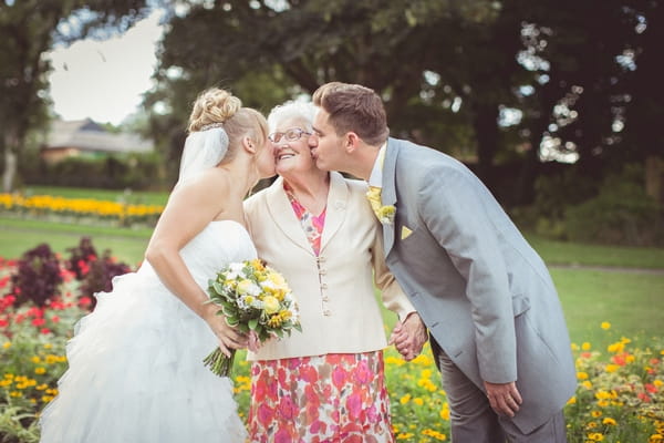 Bride and groom kiss lady on the cheeks