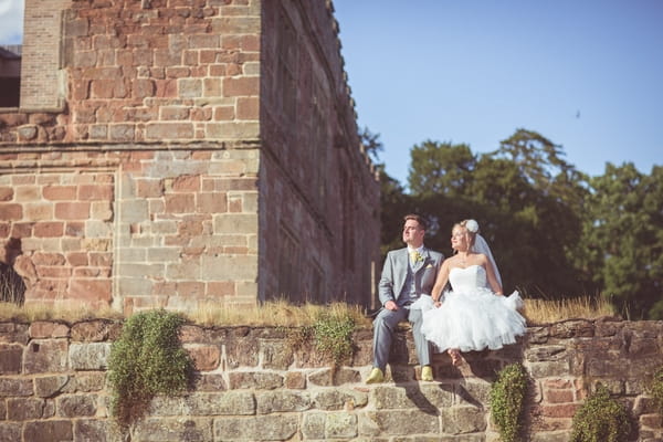 Bride and groom sitting on wall at Astley Castle