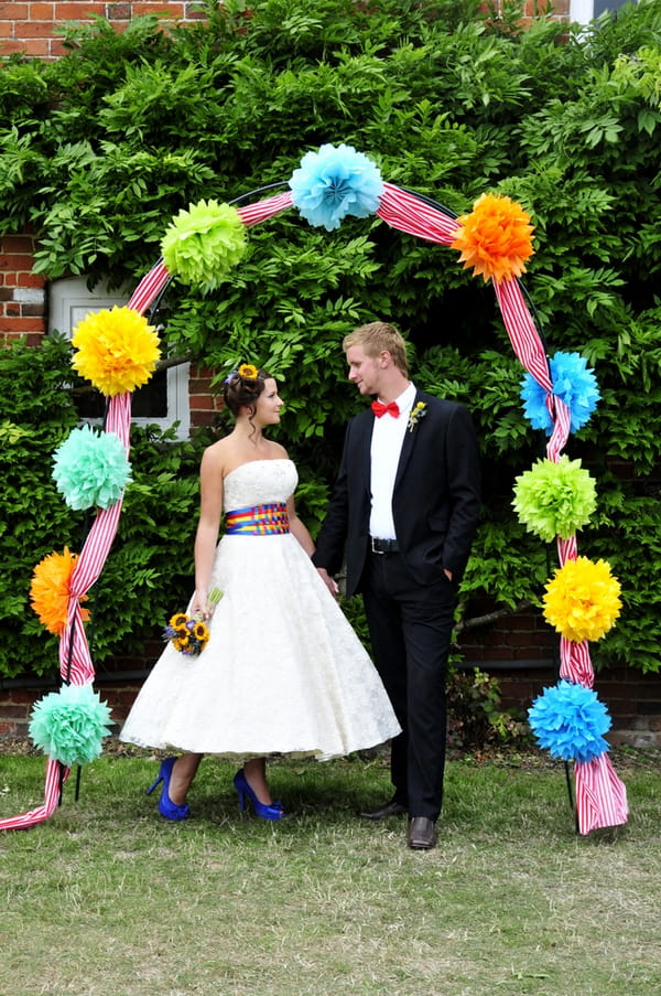 Bride and groom under arch of pom poms