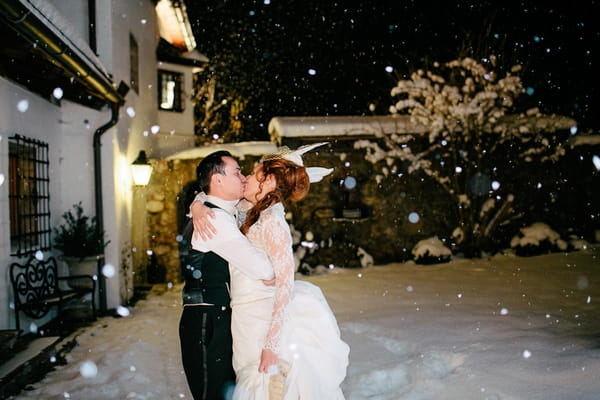 Bride and groom kiss in snow at night