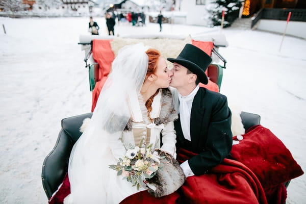 Bride and groom kiss in back of horse and carriage