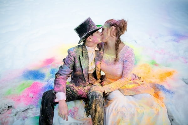 Bride and groom covered in holi powder sitting in the snow