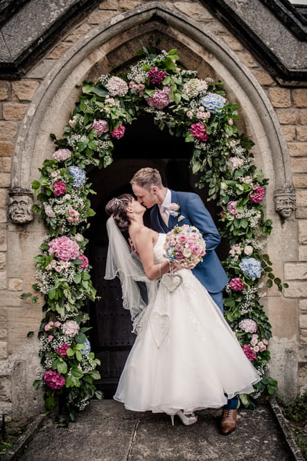 Bride and groom kissing under flower arch at church entrance