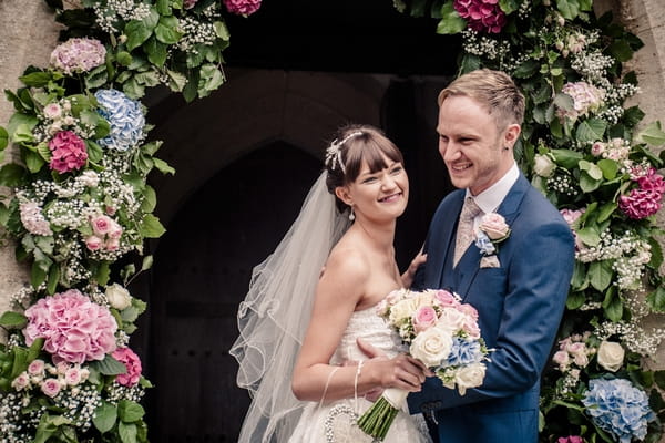 Bride and groom standing under flower arch at church entrance