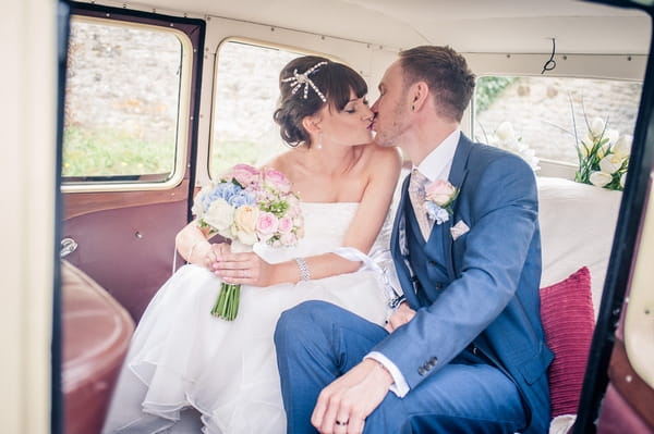 Bride and groom kiss in back of wedding car