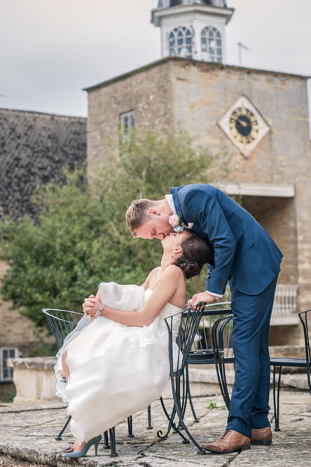 Groom kissing bride as she sits on chair