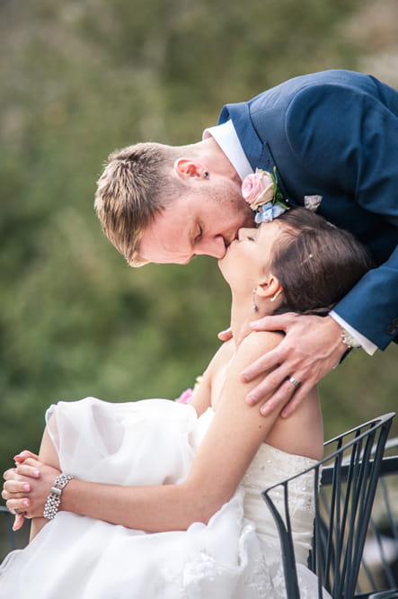 Groom kissing bride as she sits on chair