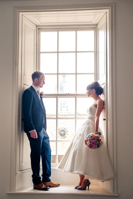 Bride and groom standing on window ledge