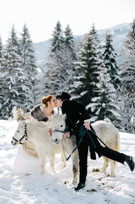 Bride and groom leaning over horses to kiss