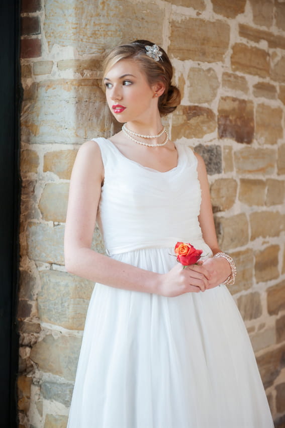 Bride holding flower and leaning against wall