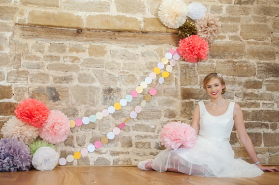 Bride sitting next to colourful paper pom poms and garland