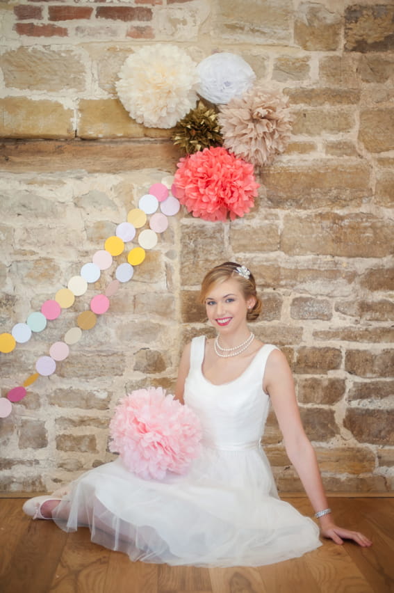 Bride sitting in front of colourful paper pom poms and garland