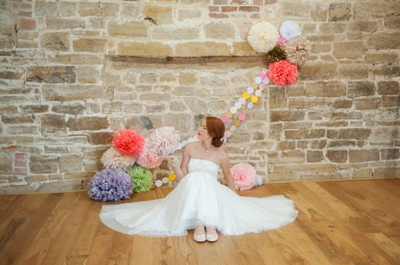 Bride sitting next to coloured paper pom poms