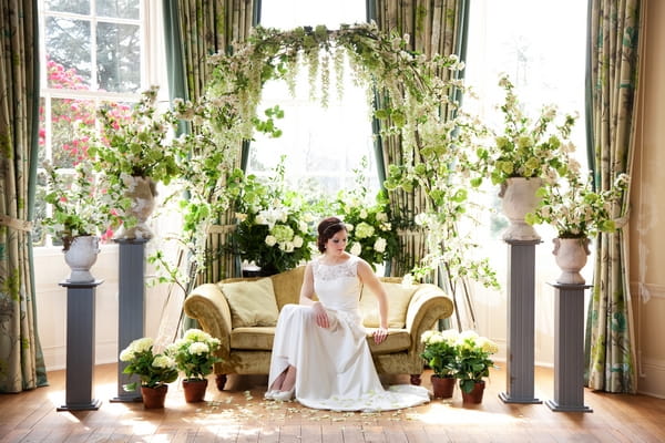 Bride sitting on sofa surrounded by spring flowers