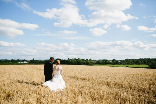 Bride and groom walking across corn field