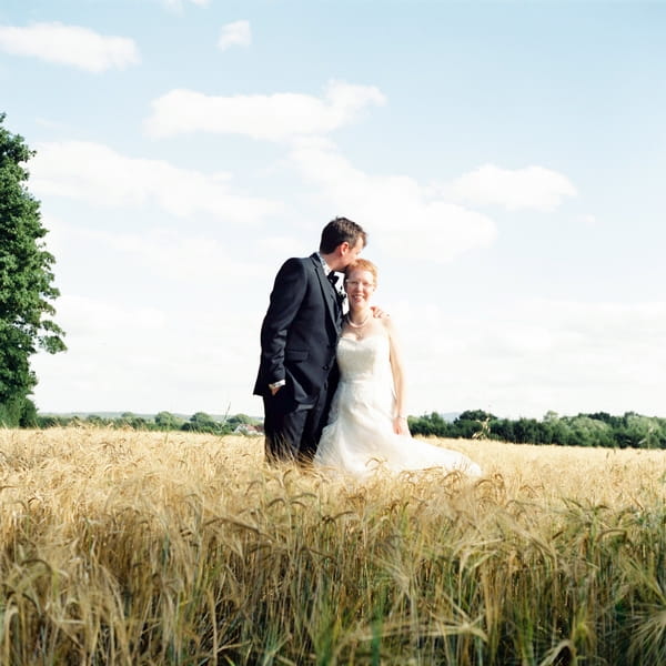 Groom kissing bride's head in corn field