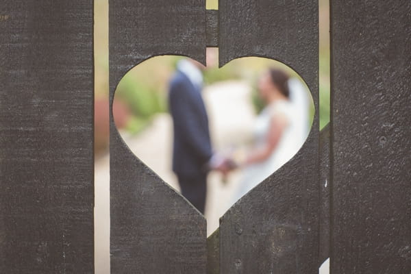 Bride and groom through heart shape in fence