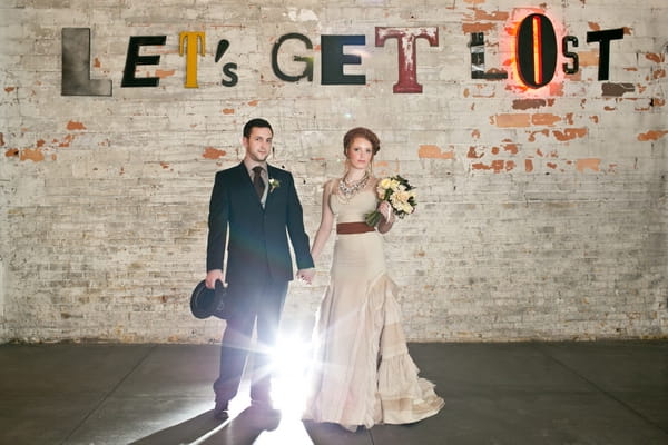 Steampunk bride and groom in front of wall with Lets Get Lost written on