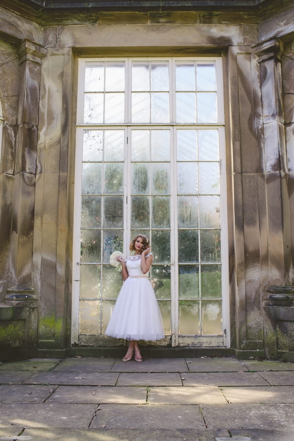 1950s bride standing in front of large glass doors