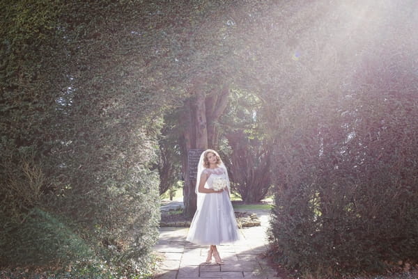 1950s bride standing under hedge