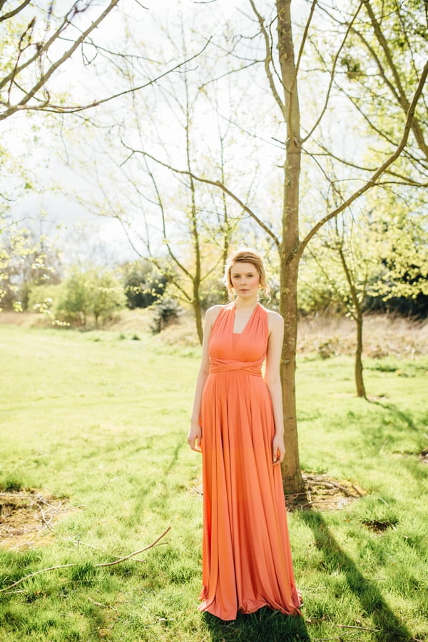 Bridesmaid in coral dress standing in front of tree