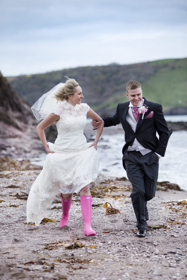 Bride in wellies and groom running on beach