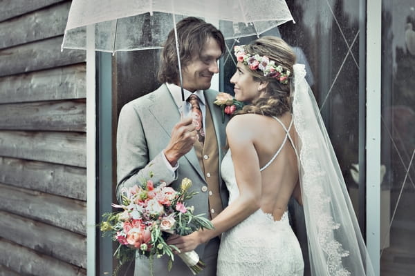 Bride and groom standing under umbrella