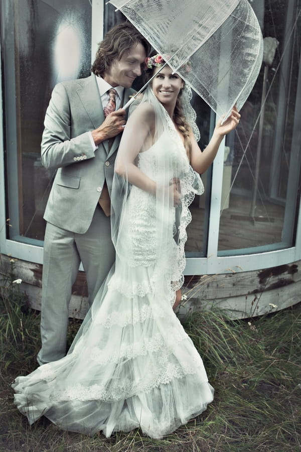 Bride and groom standing under umbrella