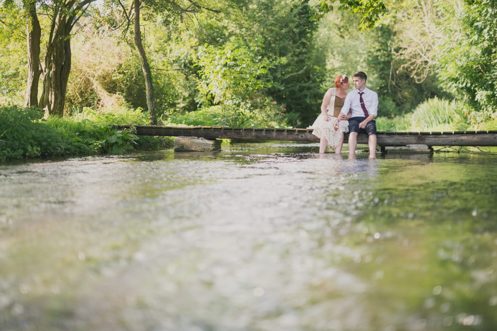 Bride and groom sitting on bridge over stream