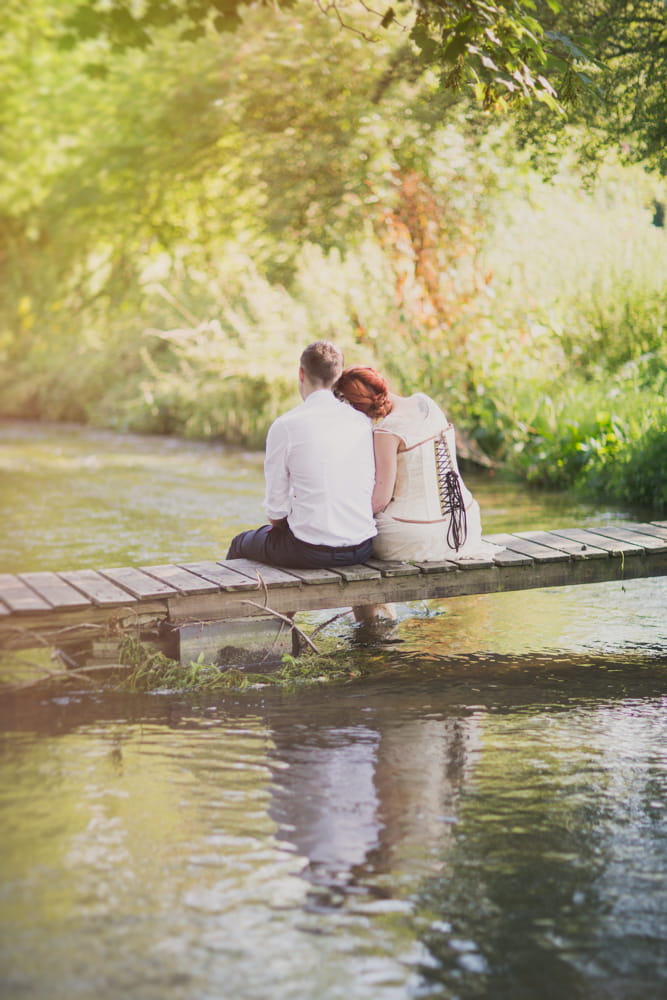 Bride and groom sitting on bridge over stream