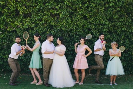 Bride, groom and bridal party holding tennis rackets