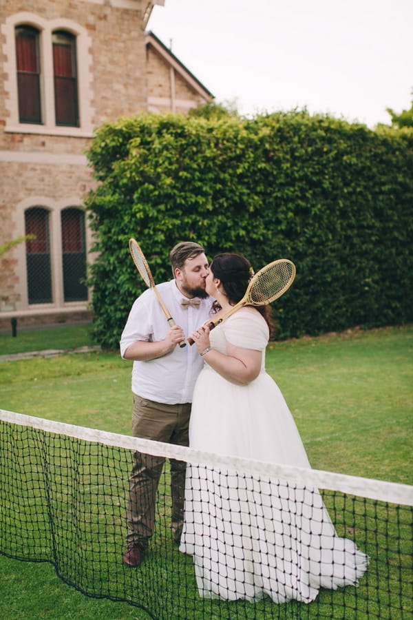 Bride and groom kissing holding tennis rackets