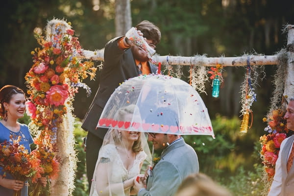 Bride and groom under umbrella in wedding ceremony