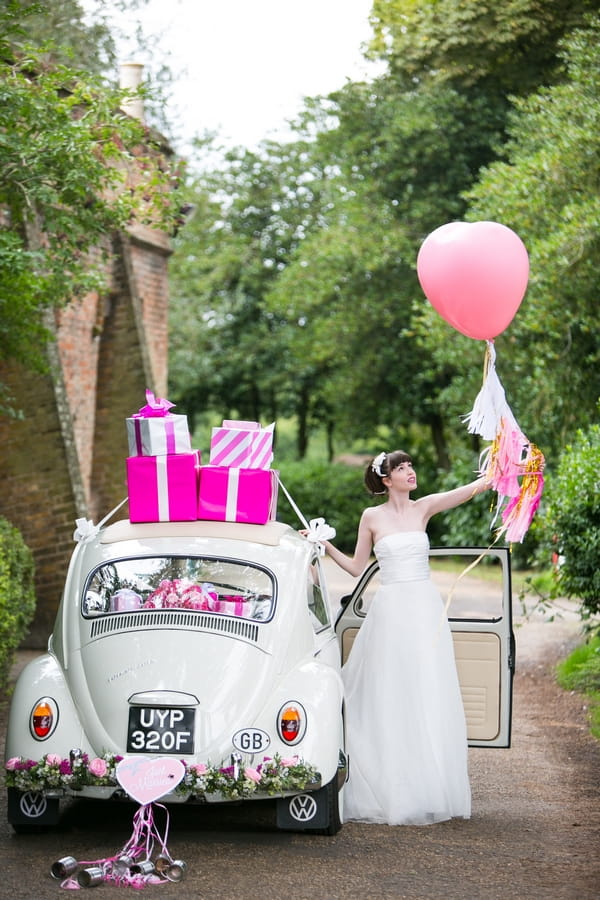 Bride holding pink balloon next to VW Beetle