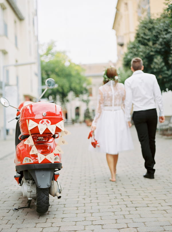 Bride and groom walking in Paris next to red Vespa